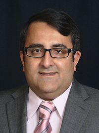 adult middle eastern man wearing black rimmed glasses, a pink shirt and tie, and a grey suit jacket