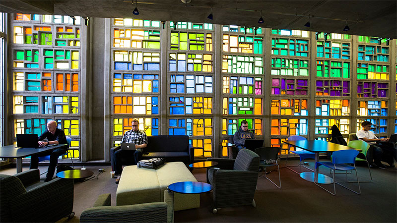 students sitting and using computers in front of very colorful stained glass